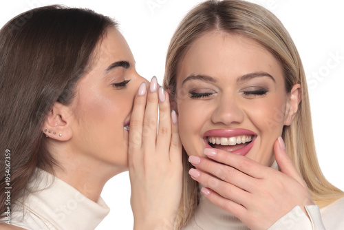 Studio shot of two young women whispering gossip secret with happy laughing expression on a white background