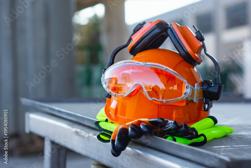 Construction safety helmet with protective goggles, gloves and reflective vest on industrial site. Concept of workplace safety, protective equipment, construction industry and labor protection.