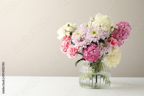 Bouquet of beautiful flowers in vase on white table against light background. Space for text