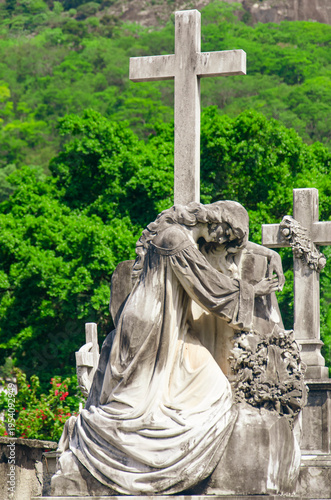 Canvas Print Female sculpture leaning on a cross, in a gesture of dejection and surrender