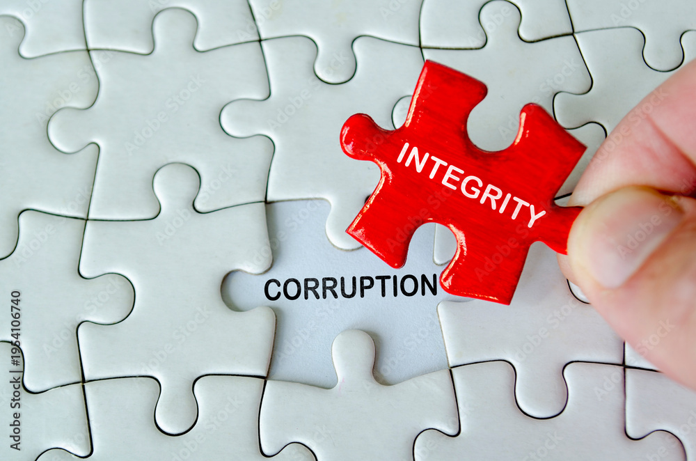 Fototapeta premium INTEGRITY and CORRUPTION, Hand holding a red integrity puzzle piece above the word compliance on a light white jigsaw puzzle background