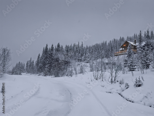 Mestervik, Norway - December 28, 2025: Just outside Malangen Brygger Resort. Snow and ice covers road up the hill where one house stands among snow-covered trees under gray sky