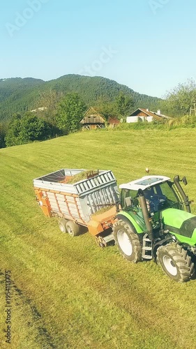 Aerial fly away while tractor loading grass on silage trailer in mountains