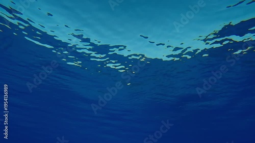 Underwater view of fine ripples on the surface of crystal clean blue water in front of a turquoise sky in calm weather. Natural undersea background of water surface in calm 