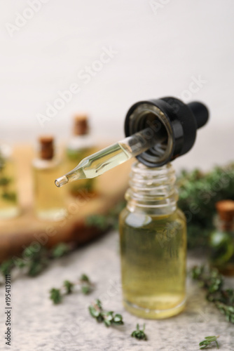 Bottles of thyme essential oil with fresh herbs and pipette on gray table, closeup