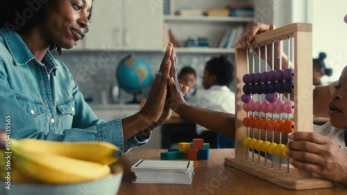 A mother and child high-five during a homeschooling math lesson using an abacus at a table. An optimistic shot of family and education. Learning together, family bonding, home schooling.