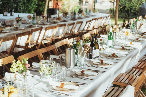 Foto Table setting, wooden folding chairs along long tables cheerfully set with decorations like flowers for dinner outdoor at daytime in summer at a wedding