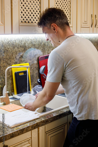 adult man washing dishes in kitchen sink under running water, household routine, cleaning process, hygiene and domestic life concept, everyday activity