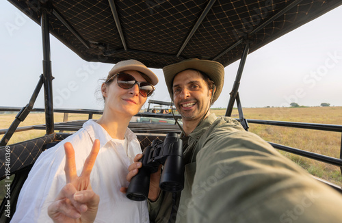 Man and a woman are sitting in a off-road car. The man is wearing a green hoodie during safari in park in South Africa