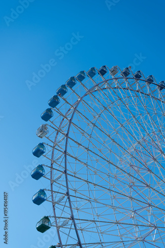 Vista vertical de la curva de una noria gigante con cabinas azules ascendiendo hacia un cielo azul despejado.
