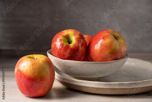 Group of red apples displayed on a plate and bowl in a minimalist kitchen setting with soft light