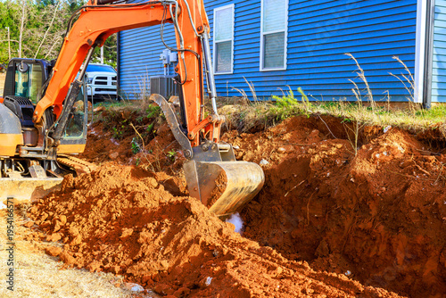 Excavator digs trench near building in residential construction area