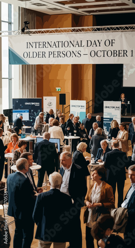 People attend older adults conference, engaging in discussions and networking inside large hall. Event promotes senior engagement for International Day of Older Persons.