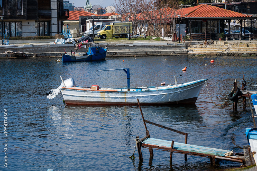 Obraz premium a traditional white and blue wooden fishing boat moored in a calm harbor, featuring a rustic wooden and metal pier in the foreground 