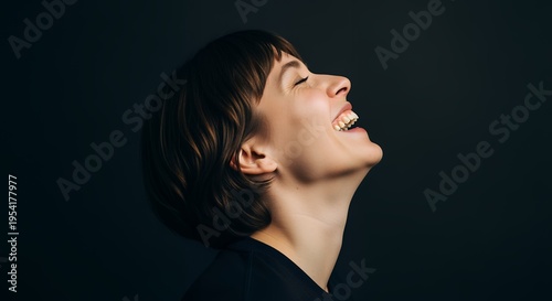 Joyful young woman laughing with eyes closed and head tilted back against a dark background, expressing pure happiness and positive emotion.