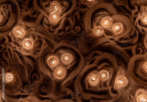 Top view of small candle lights glowing in sculpted brown sand 