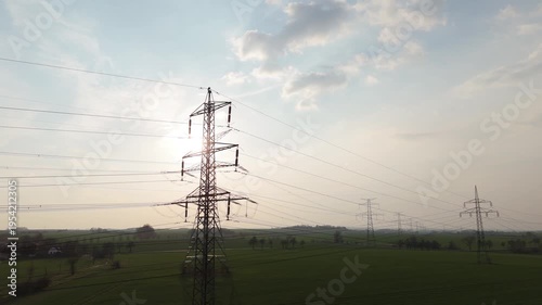 Aerial drone rising shot of high voltage electricity pylons row across green fields at sunset