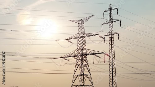 Aerial drone orbit around high voltage electricity pylons silhouette against sunset sky