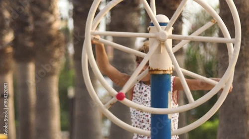 Little girl rotates a metal circle on the playground in the city.