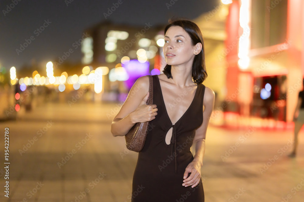 Fototapeta premium Woman walks in vicinity of Passeig de Sant Joan, spend time in public urban space. Atmosphere of relaxation, idleness, entertainment. Electric street lighting, night life in big city