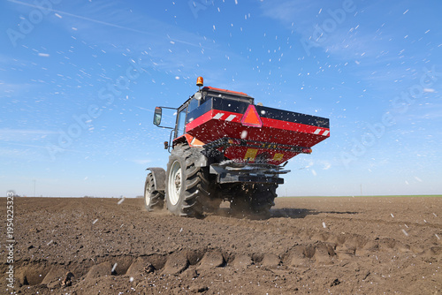 Spreading mineral fertilizer, low angle shot. Farmer with agricultural machinery fertilizing agricultural field in spring time.