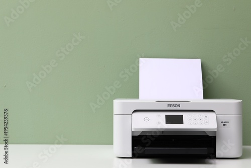 One printer with sheet of paper on white table near green wall, closeup. Space for text