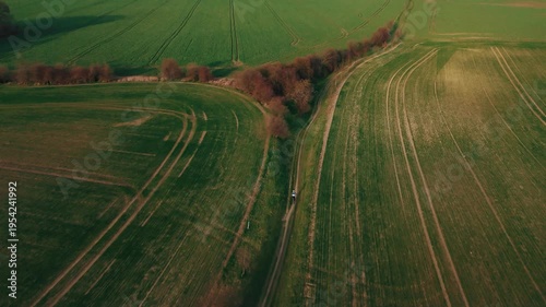 Aerial drone following cyclist on rural path through green fields at golden hour