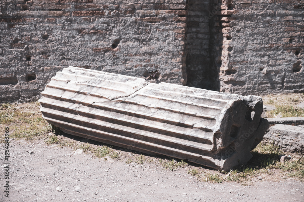 Obraz premium An ancient column lies on the ground among the remains of a structure. The column shows signs of wear with detailed grooves and is part of a historic site.