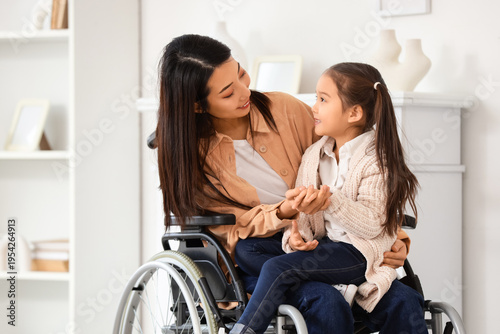 Photos Young Asian mother in wheelchair with her little daughter holding hands at home