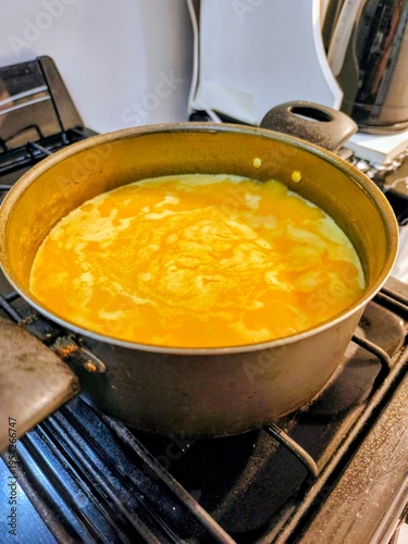 close view of boiling pumpkin and cream soup in a metal pot on top of a stove