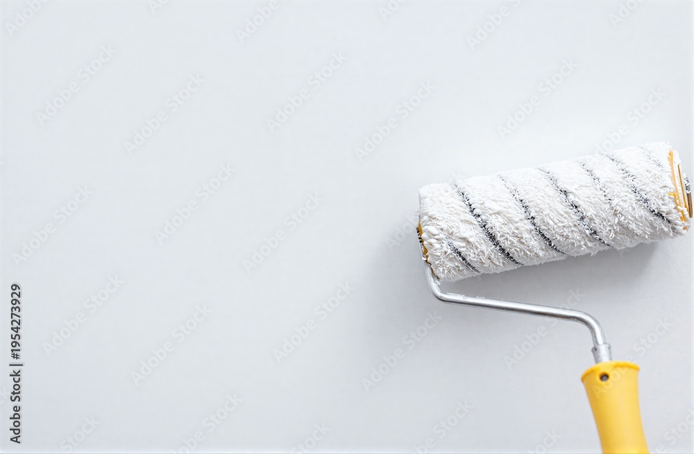 Obraz premium Paint roller with yellow handle rests against a plain white wall.