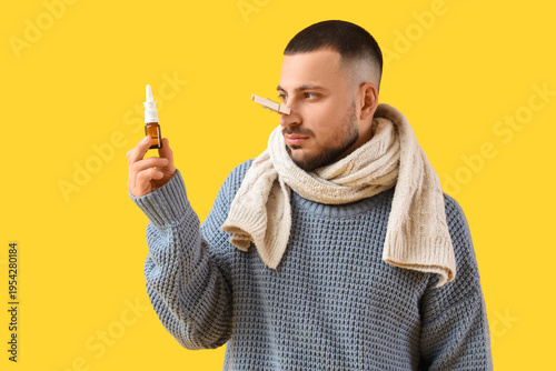 Canvastavla Ill young man with clothespin and nasal drops on yellow background