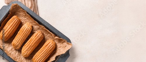 Obraz na płótnie Baking dish with tasty eclairs on light grunge background