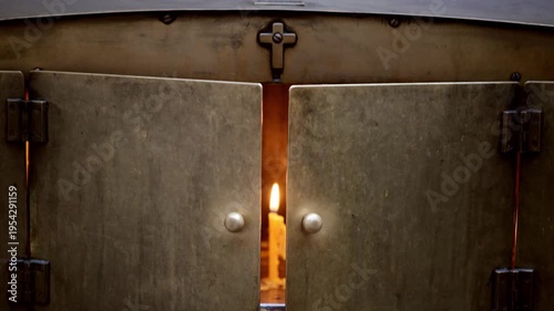 A candle burns softly, casting warm light through the gap of heavy metal doors