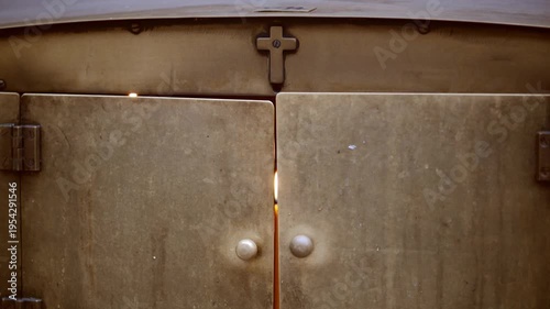 A candle burns softly, casting warm light through the gap of heavy metal doors