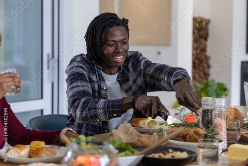 Diverse couple sitting at dining table, African American adult male carving roast with knife fork