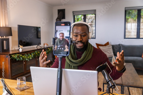 African American man in 30s sitting at living room desk recording with laptop phone tripod mic
