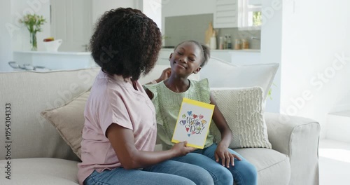 African American mom and child sitting on sofa mom showing yellow card for Mother's Day hugging