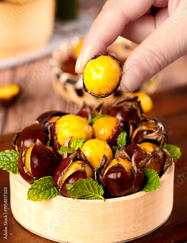 Fresh Roasted Chestnuts in Wooden Bowl with Hand Picking Delicious Autumn Nuts