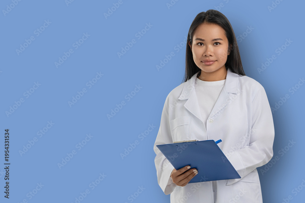 Obraz premium Medical worker in white coat stands holding clipboard