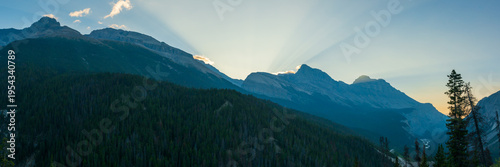 Panoramic mountain sunrise with dramatic sun rays over the pine forests and peaks along the Icefields Parkway in the Canadian Rockies, Alberta.
