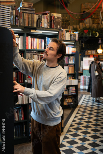 Fotografie Intelligent focused man booklover searching books and publications from shelf in trendy bookstore