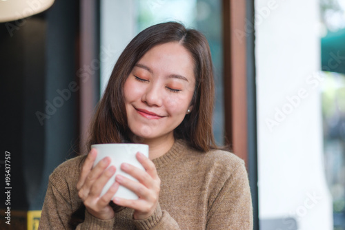 Portrait image of a woman with closed eyes holding and drinking hot coffee