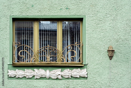 Rectangular window with a yellow frame and an openwork grille featuring white moldings against a green wall. From the series of windows of St. Petersburg.