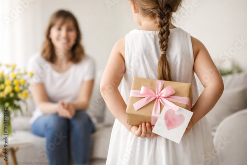 Little girl hiding gift box and card behind back for mother