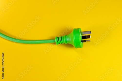 Closeup of a green Australian electricity cord plug socket on a yellow background. This electrical power cable illustrates the concept of expensive energy and bill cost savings.