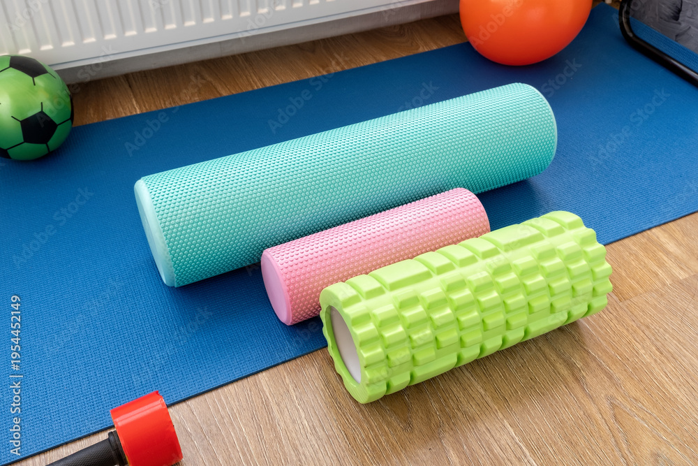Obraz premium Different types of foam rollers and equipment on blue exercise mat in gym area at home