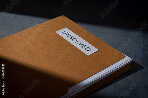 Brown manila folder with UNSOLVED label on a dark surface. Mystery, cold cases, criminal investigation, and unresolved problems concept.