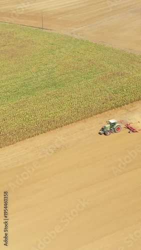 Drone shot of a tractor working on a large agricultural field, with crops and tilled soil visible. Ideal for illustrating modern farming and rural landscapes.
