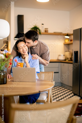 Couple shares a moment in kitchen while working on a laptop and enjoying a drink